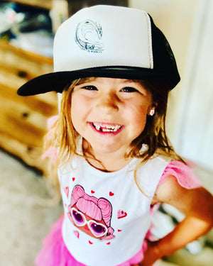 Child wearing a white and black cap with a logo, smiling outdoors.