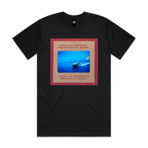 Black t-shirt with a graphic design of a ship in the ocean and 'Creative Freedom Processed by Kodak' text on a white background.