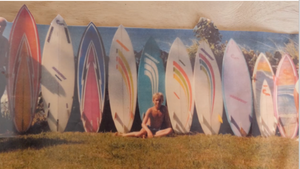 Man sitting among surfboards with a colorful background