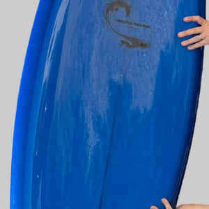 Blue surfboard held by a person against a gray background