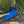 Person holding a blue kayak on a path with trees in the background