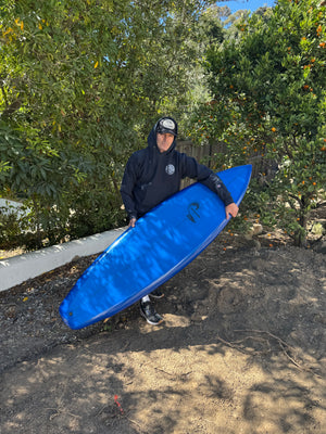 Person holding a blue kayak on a path with trees in the background