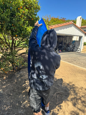 Person holding a blue object outdoors with trees and a building in the background