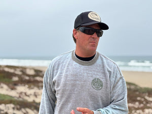 Man wearing sunglasses and a cap with a beach in the background