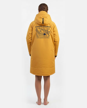 Woman wearing a mustard yellow coat with a brand logo on the back against a white background